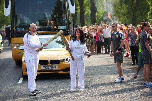 Torchbearer 015 Louise Brown passes the Olympic Flame to Torchbearer 016 Ian Dugmore on the Torch Relay leg between Malvern and Malvern Wells