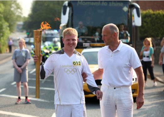 Torchbearer 012 Daniel Johnsey and his chaperone, his uncle, Steven Flynn, passes the Olympic Flame to Torchbearer 013 Richard Brown on the Torch Relay leg between Malvern and Malvern Wells