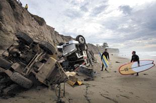 Surfers walk past a truck on the beach at the base of Silver Shoals Drive in Pismo Beach, California