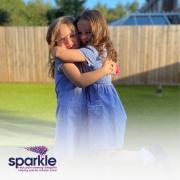 Two children hugging, one that attends Sparkle services, together with her sister.