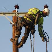 An archive photograph of a workman repairing a high voltage overhead line.